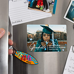 Custom graduation photo magnet displayed on a stainless steel refrigerator showing a graduate in cap and gown blowing confetti with personalized name, university, and class year text