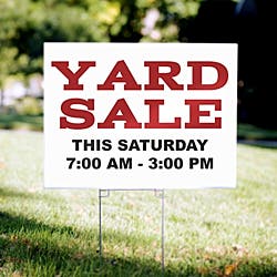 Corrugated plastic yard sign installed on a stake in a yard with printed content advertising a yard sale and a date and time. 