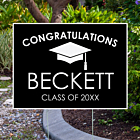 Simple black graduation yard sign with bold white text showing graduate name and class year displayed in front yard