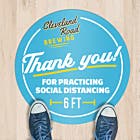 A blue circle floor sticker for a brewing company applied to a wood floor thanking people for social distancing of 6 feet.