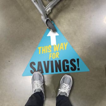 Triangle Floor Sticker applied to a concrete floor with text that reads this way for savings.