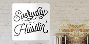 An aluminum sign that says Everyday I'm Hustlin applied to a brick wall just above a decorative side table.  