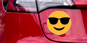 A smiley face magnet applied to the trunk of a red car.