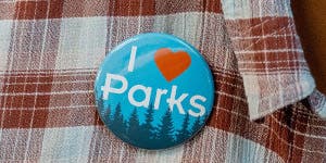 A button applied to someones shirt that reads, "I love parks" with a forest skyline. 